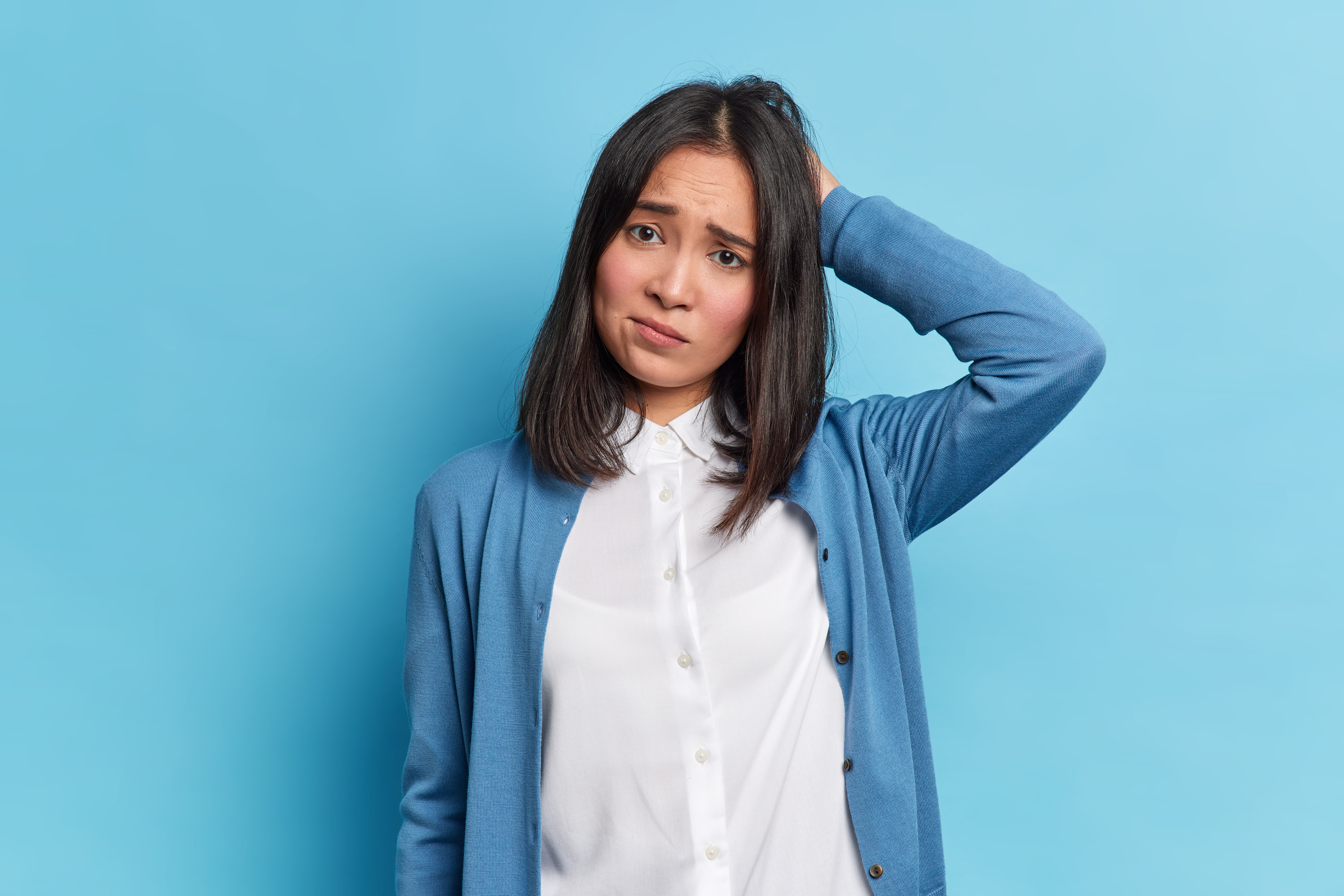 disappointed grumpy brunette young woman with eastern appearance scratches head frowns face looks unhappily camera wears white shirt blue jumper poses indoor negative emotions concept 10 Lý do gây rụng tóc ở Phụ nữ sau tuổi 30 Go1Care